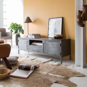 Vandana Cresta Arion – Gustavo Industrial TV Stand in Mango Wood & Grey Metal is a perfect balance of industrial character, smart storage, and modern functionality. Designed for contemporary interiors that value both aesthetics and practicality, this TV stand combines robust materials with a refined, structured layout to create a visually striking yet highly usable media unit. The design features a strong frame crafted entirely from grey metal, giving the unit a bold industrial presence. This is beautifully contrasted by a solid mango wood top finished with a subtle whitewashed grey patina, adding warmth and brightness to the overall look. The blend of metal and wood creates a timeless industrial appeal that fits seamlessly into loft-style apartments, modern homes, and urban interiors. Measuring 150 cm in width, this TV stand offers an ideal footprint for both compact apartments and spacious family living rooms. Its intelligently designed storage system ensures excellent organization. The unit includes two metal doors inspired by vintage locker designs, adding a distinctive industrial charm while concealing generous storage space for books, DVDs, games, and accessories. A central drawer provides additional enclosed storage for smaller items, while the open niche is perfect for multimedia devices, decorative objects, or sound systems. The open compartment also allows for efficient cable management, helping you maintain a clean and clutter-free entertainment area. With a height of 47.5 cm and a depth of 40.5 cm, the unit offers comfortable viewing proportions while remaining visually balanced and space-efficient. Crafted from solid mango wood, known for its durability and low maintenance, this TV stand is built for long-term everyday use. Delivered fully assembled, it ensures immediate installation with no effort required. As part of the Gustavo collection, it can be easily paired with matching furniture pieces to create a cohesive industrial interior while benefiting from optimized shipping solutions. Durable, functional, and stylish, the Vandana Cresta Arion TV stand is an excellent choice for those seeking industrial design with refined storage solutions and lasting quality.