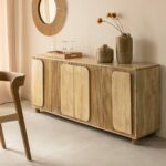 The Vandana Prime Stellar – Eros Sideboard is a striking expression of originality, craftsmanship, and contemporary design, expertly crafted from solid mango wood. Designed to stand out while remaining functional, this sideboard combines sculptural aesthetics with everyday practicality, making it an exceptional centerpiece for modern interiors. Entirely constructed from high-quality mango wood, the Eros sideboard showcases the natural beauty of the material through its rich grain patterns, warm golden tones, and durable structure. Mango wood is valued not only for its visual appeal but also for its strength and longevity, ensuring this piece will remain a part of your interior for many years to come. What truly sets the Eros sideboard apart is its textured, vertically slatted door fronts, enhanced by applied rounded panels that soften the linear design. This thoughtful combination of graphic lines and curved elements creates a dynamic visual rhythm, giving the furniture a strong and recognizable identity. The sculpted detailing adds depth and character, reflecting refined contemporary craftsmanship. Behind its four hinged doors, the sideboard offers generous internal storage space, ideal for organizing dishes, tableware, linens, books, or everyday essentials. Its spacious top surface allows you to display decorative objects, vases, lamps, or art pieces, further enhancing the atmosphere of your living or dining area. With dimensions of 175 cm width, 77 cm height, and 40 cm depth, the Eros sideboard provides ample storage while maintaining a balanced and elegant silhouette. It integrates seamlessly into modern, bohemian chic, or wabi-sabi inspired interiors, where natural materials and organic forms are celebrated. Delivered fully assembled, this sideboard offers immediate usability and reflects export-quality manufacturing standards, making it suitable for residential projects, hospitality spaces, boutique hotels, and premium interior concepts. The Vandana Prime Stellar – Eros Mango Wood Sideboard is more than a storage unit—it is a statement of design, texture, and authenticity, created for buyers who value originality, natural materials, and timeless elegance.