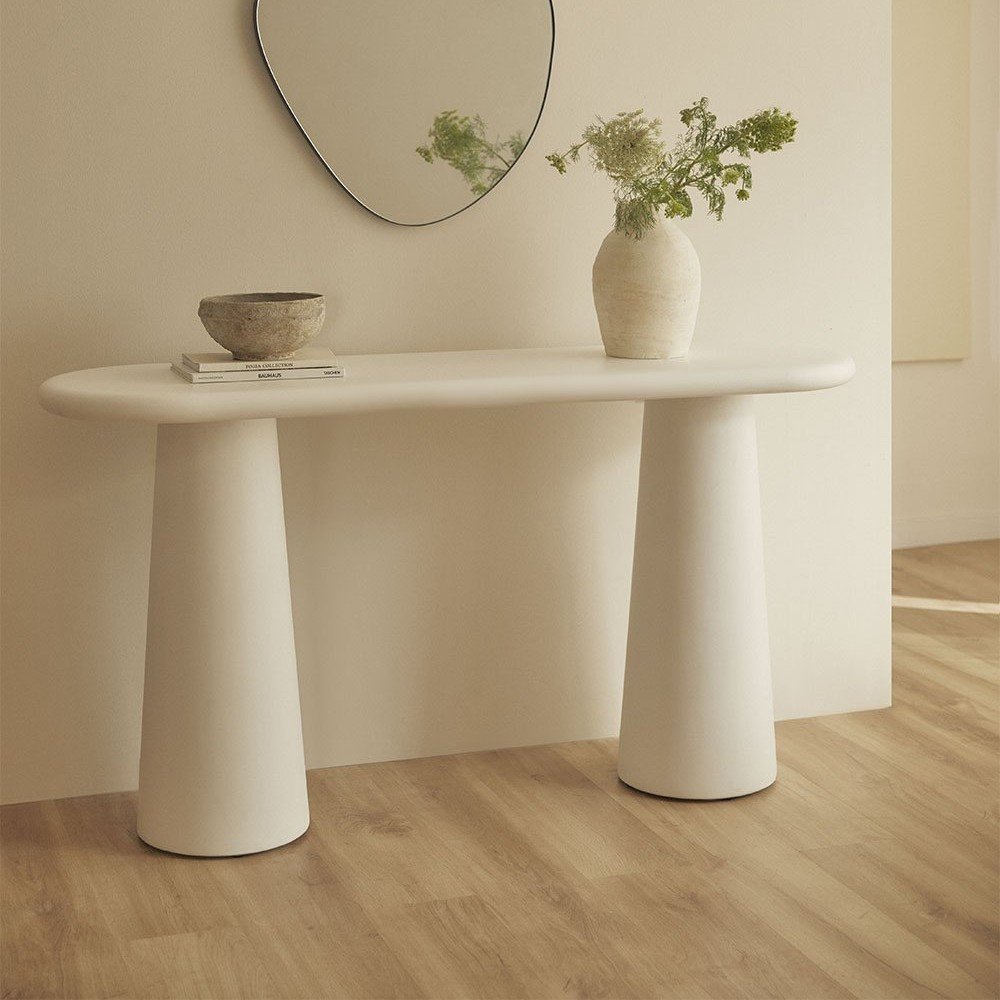Vandana Terra Flux Cement Console Table is a bold and contemporary statement piece designed to bring architectural elegance and functional strength into modern interiors. Crafted for refined living spaces, this console table combines minimalist aesthetics with advanced material engineering, making it an ideal addition to entryways, living rooms, corridors, and high-end hospitality environments. Constructed from premium fiberglass-reinforced cement, the Noemi console offers exceptional durability while maintaining a clean, sculptural appearance. This innovative material provides high resistance to impact, moisture, and daily wear, ensuring long-term stability even in demanding environments. The console is finished with a specialized paint-based protective coating that creates an anti-stain barrier, enhances surface durability, and protects the structure in high-humidity conditions. The wide, flat tabletop offers generous space for decorative objects, lighting, art pieces, or everyday essentials, making the console both functional and visually striking. Its neutral cement tone allows it to blend effortlessly with modern, minimalist, industrial, and contemporary interior styles, while its sculptural presence adds character without overwhelming the space. The legs feature a slightly tapered yet robust design, ensuring excellent balance and structural integrity. Integrated protective pads on the base safeguard flooring surfaces from scratches and marks, making the console suitable for marble, wood, and tiled floors. Each console may display subtle tonal and textural variations, highlighting the natural character of cement and reinforcing its artisanal appeal. With its refined proportions and architectural lines, the Vandana Terra Flux console is perfectly suited for luxury homes, boutique hotels, serviced apartments, and contract projects seeking durable designer furniture. Built to export-quality standards, this cement console table is not only a functional furnishing but a statement of modern design, strength, and understated sophistication. Vandana Terra Flux cement console