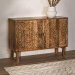 The Vandana Grand Optima 105x35 cm Sideboard in Wiluna Mango Wood is a refined storage piece that brings warmth, craftsmanship, and artistic character into your home. Handcrafted from premium solid mango wood, this sideboard is designed to enhance interiors with its natural beauty, durability, and timeless appeal. Its compact proportions make it ideal for modern homes while still offering practical storage solutions. Finished in a natural wood tone, the Grand Optima sideboard highlights the rich grain patterns and organic textures of mango wood. Known for its strength and resistance, mango wood ensures long-lasting performance, making this sideboard suitable for everyday use in living rooms, hallways, or bedrooms. The natural finish allows the material to breathe, creating a warm and inviting atmosphere that blends effortlessly with contemporary, rustic, or traditional décor styles. The standout feature of this piece is its hand-carved floral detailing, which adds depth, texture, and a distinctive boho-chic character. These delicate motifs give the sideboard an artisanal identity, transforming it from a simple storage unit into a decorative focal point. Each carved pattern is unique, reflecting skilled craftsmanship and ensuring that no two pieces are exactly alike. Despite its slim depth of 35 cm, the sideboard offers generous internal storage for organizing everyday essentials such as books, accessories, tableware, or personal items. Its balanced structure feels visually light yet robust in construction, making it both practical and aesthetically pleasing. Raised on sturdy legs with a height of 17.5 cm, the sideboard allows easy floor cleaning while maintaining a refined silhouette. As mango wood is a natural material, variations in colour may range from warm browns and golden hues to subtle yellow, red, or darker accents. These variations are part of the authentic charm of solid wood furniture. To preserve its beauty and durability, it is recommended to follow wood-specific care instructions and avoid harsh chemical cleaners. The Vandana Grand Optima Sideboard is a perfect choice for those seeking handcrafted wooden furniture that combines bohemian elegance, functionality, and lasting quality—bringing personality and warmth into every corner of your home.