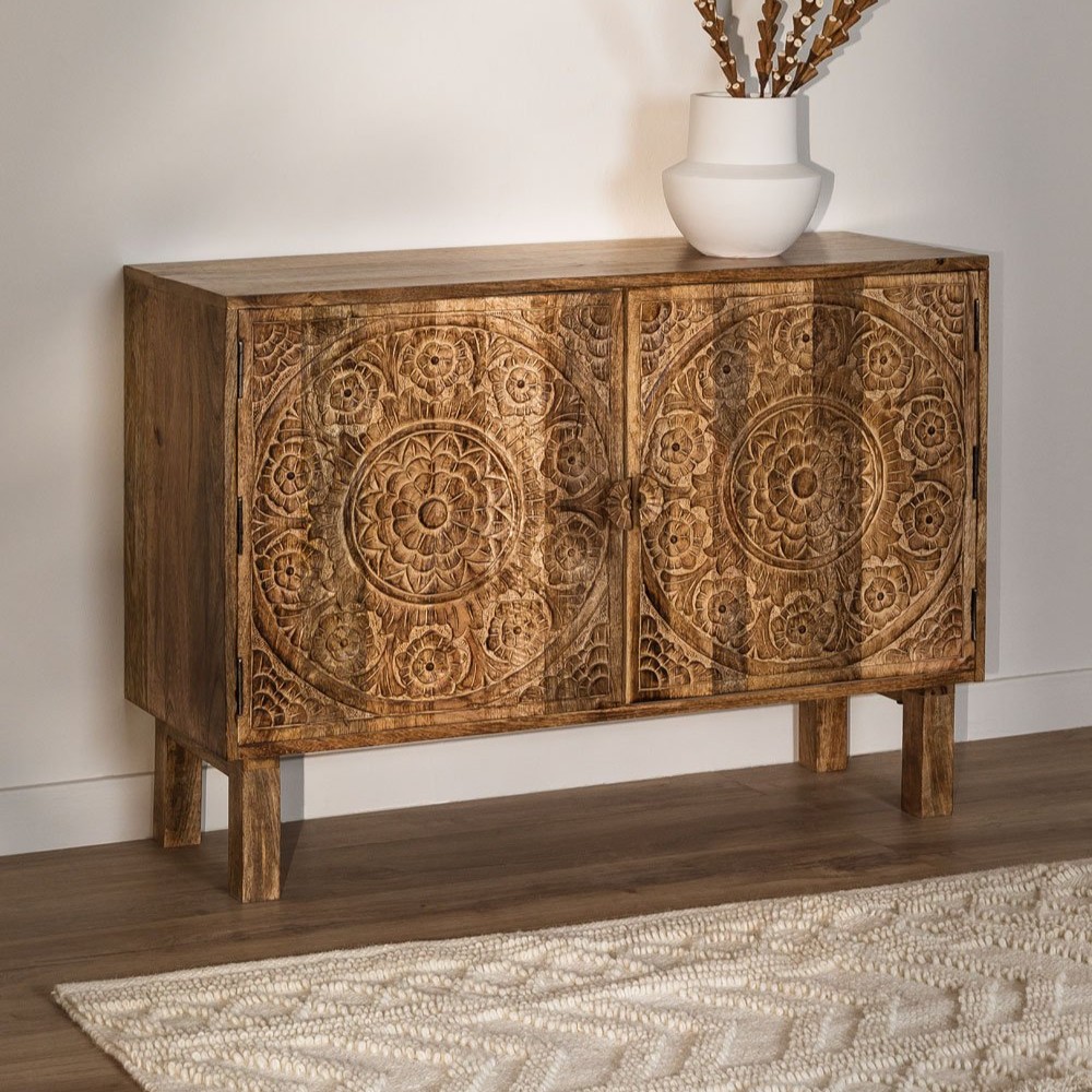 The Vandana Grand Optima 105x35 cm Sideboard in Wiluna Mango Wood is a refined storage piece that brings warmth, craftsmanship, and artistic character into your home. Handcrafted from premium solid mango wood, this sideboard is designed to enhance interiors with its natural beauty, durability, and timeless appeal. Its compact proportions make it ideal for modern homes while still offering practical storage solutions. Finished in a natural wood tone, the Grand Optima sideboard highlights the rich grain patterns and organic textures of mango wood. Known for its strength and resistance, mango wood ensures long-lasting performance, making this sideboard suitable for everyday use in living rooms, hallways, or bedrooms. The natural finish allows the material to breathe, creating a warm and inviting atmosphere that blends effortlessly with contemporary, rustic, or traditional décor styles. The standout feature of this piece is its hand-carved floral detailing, which adds depth, texture, and a distinctive boho-chic character. These delicate motifs give the sideboard an artisanal identity, transforming it from a simple storage unit into a decorative focal point. Each carved pattern is unique, reflecting skilled craftsmanship and ensuring that no two pieces are exactly alike. Despite its slim depth of 35 cm, the sideboard offers generous internal storage for organizing everyday essentials such as books, accessories, tableware, or personal items. Its balanced structure feels visually light yet robust in construction, making it both practical and aesthetically pleasing. Raised on sturdy legs with a height of 17.5 cm, the sideboard allows easy floor cleaning while maintaining a refined silhouette. As mango wood is a natural material, variations in colour may range from warm browns and golden hues to subtle yellow, red, or darker accents. These variations are part of the authentic charm of solid wood furniture. To preserve its beauty and durability, it is recommended to follow wood-specific care instructions and avoid harsh chemical cleaners. The Vandana Grand Optima Sideboard is a perfect choice for those seeking handcrafted wooden furniture that combines bohemian elegance, functionality, and lasting quality—bringing personality and warmth into every corner of your home. The Vandana Grand Optima 105x35 cm Sideboard in Wiluna Mango Wood is a refined storage piece that brings warmth, craftsmanship, and artistic character into your home. Handcrafted from premium solid mango wood, this sideboard is designed to enhance interiors with its natural beauty, durability, and timeless appeal. Its compact proportions make it ideal for modern homes while still offering practical storage solutions. Finished in a natural wood tone, the Grand Optima sideboard highlights the rich grain patterns and organic textures of mango wood. Known for its strength and resistance, mango wood ensures long-lasting performance, making this sideboard suitable for everyday use in living rooms, hallways, or bedrooms. The natural finish allows the material to breathe, creating a warm and inviting atmosphere that blends effortlessly with contemporary, rustic, or traditional décor styles. The standout feature of this piece is its hand-carved floral detailing, which adds depth, texture, and a distinctive boho-chic character. These delicate motifs give the sideboard an artisanal identity, transforming it from a simple storage unit into a decorative focal point. Each carved pattern is unique, reflecting skilled craftsmanship and ensuring that no two pieces are exactly alike. Despite its slim depth of 35 cm, the sideboard offers generous internal storage for organizing everyday essentials such as books, accessories, tableware, or personal items. Its balanced structure feels visually light yet robust in construction, making it both practical and aesthetically pleasing. Raised on sturdy legs with a height of 17.5 cm, the sideboard allows easy floor cleaning while maintaining a refined silhouette. As mango wood is a natural material, variations in colour may range from warm browns and golden hues to subtle yellow, red, or darker accents. These variations are part of the authentic charm of solid wood furniture. To preserve its beauty and durability, it is recommended to follow wood-specific care instructions and avoid harsh chemical cleaners. The Vandana Grand Optima Sideboard is a perfect choice for those seeking handcrafted wooden furniture that combines bohemian elegance, functionality, and lasting quality—bringing personality and warmth into every corner of your home.
