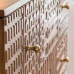 The Vandana Ultra Grand Leopold Carved Mango Wood Chest of Drawers is a timeless statement piece that blends authentic craftsmanship with refined contemporary accents. Expertly crafted from premium solid mango wood and elevated on elegant gold-tone metal legs, this chest of drawers brings warmth, character, and sophistication to modern living spaces. With balanced dimensions of 92 cm in height, 90 cm in width, and 40 cm in depth, the Leopold chest offers generous storage while maintaining a compact and harmonious silhouette. Its proportions make it an excellent choice for bedrooms, living rooms, dining areas, or entryways, where it functions as both a practical organizer and a decorative focal point. The defining feature of this piece is its beautifully carved door motif, which adds texture and artisanal depth while preserving a clean and minimal aesthetic. The carved detailing reflects skilled workmanship and highlights the natural beauty of mango wood, known for its warm tones and expressive grain. Each piece showcases subtle variations in color and pattern, ensuring a unique, handcrafted identity. Designed for everyday functionality, the chest provides ample internal storage space to neatly organize clothing, linens, accessories, documents, or household essentials. Its thoughtful layout allows for easy organization while keeping interiors clutter-free. The sturdy solid wood construction ensures durability and long-term stability, making this furniture suitable for daily use over many years. The gold-finish metal legs add a contemporary touch and visually lighten the structure, creating an elegant contrast with the warmth of the wood. These refined accents elevate the overall design, allowing the chest to blend seamlessly into authentic, modern, or transitional interiors. The result is a piece that feels both classic and current. Delivered fully assembled, only the screw-in feet need to be attached using the provided instructions, making installation quick and simple. Securely packaged for safe transport, the Vandana Ultra Grand Leopold Chest of Drawers is ready to enhance your interior upon arrival. A true expression of style and craftsmanship, it is designed to bring lasting beauty and functionality to your home.
